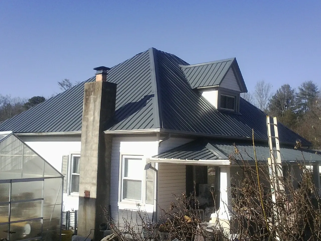 Dark blue standing seam metal roof on a white farmhouse with dormer — Slate & Tile Roof Repair by Roofing Brothers in Hiddenite