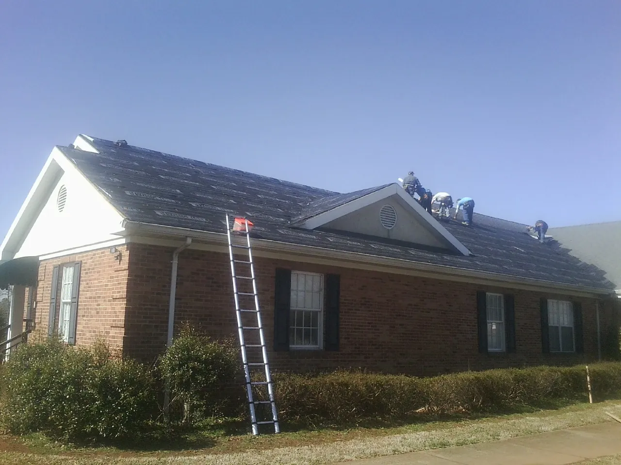 Crew tearing shingles off a brick ranch roof with a ladder set — Emergency Roof Repair work by our crew in Hiddenite