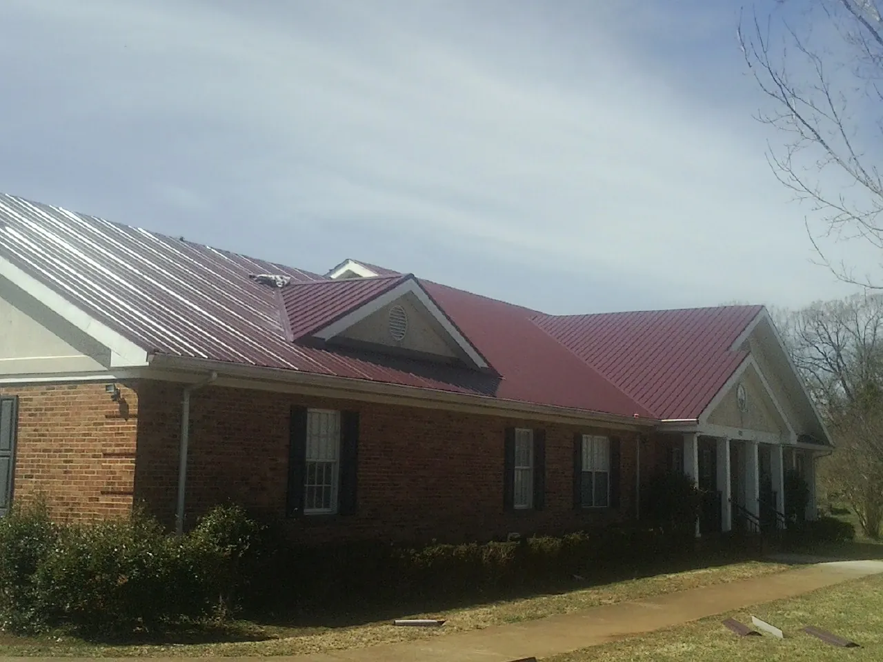 Red metal roof with gabled entries on a long brick building, from a Hail Damage Roof Repair job in Hiddenite