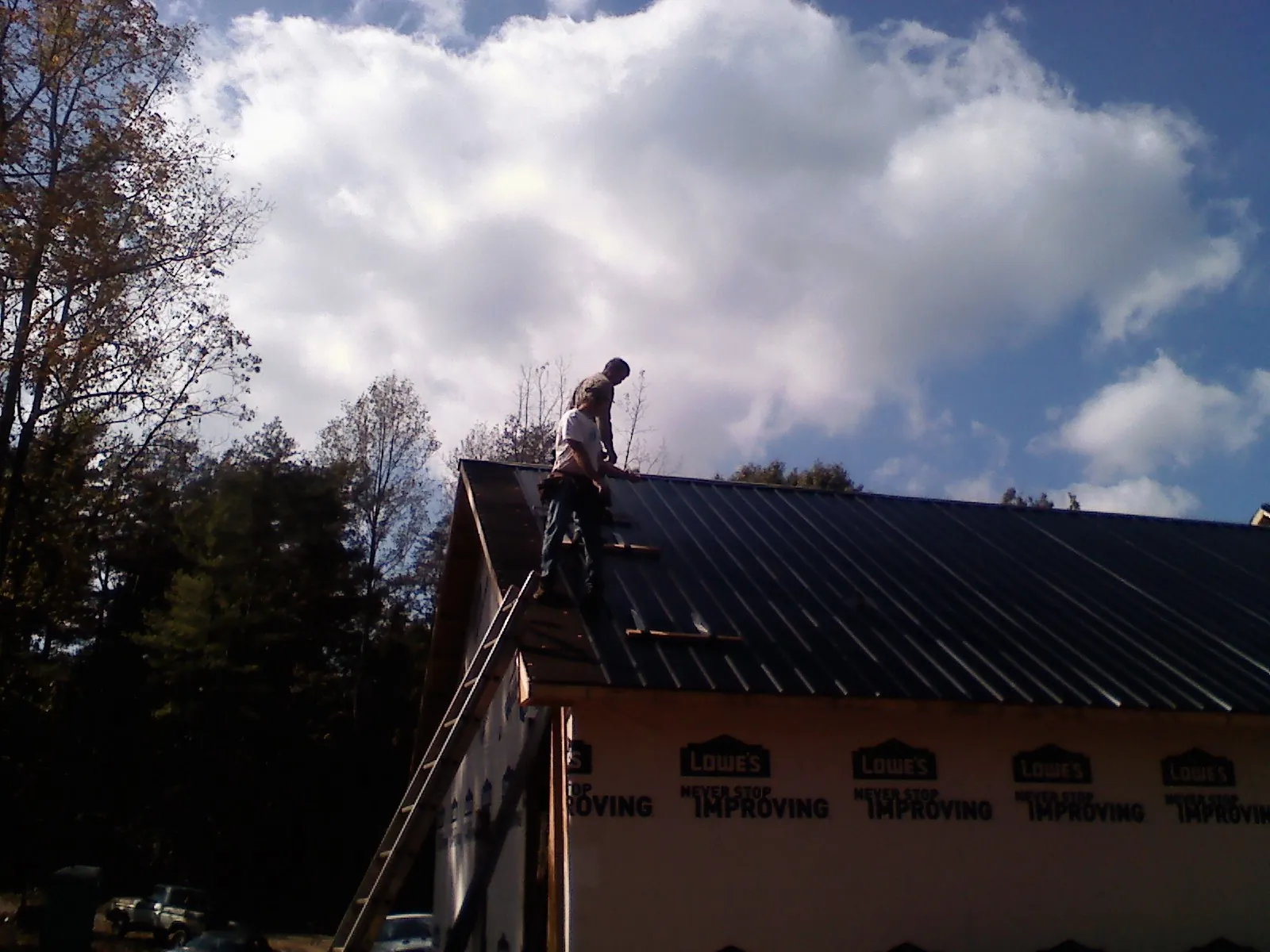 Roofer fastening dark metal panels high against a cloudy sky, from a Roof Inspection job in Hiddenite