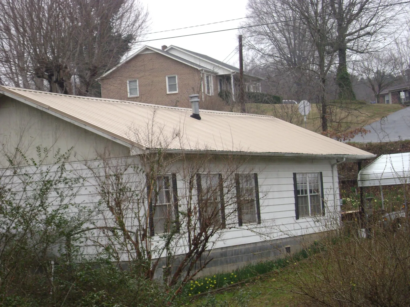 Tan metal roof on a white sided house set into a hillside — Commercial Roofing by Roofing Brothers in Hiddenite