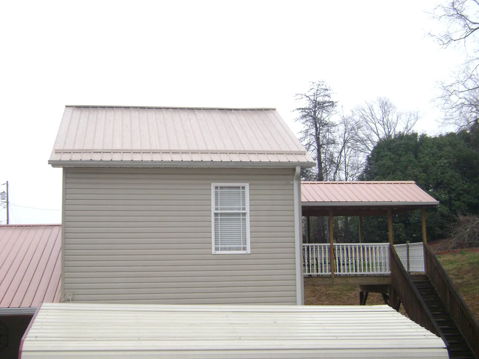 Tan metal roofs on a two story addition and attached porch, from a Roof Replacement job in Hiddenite